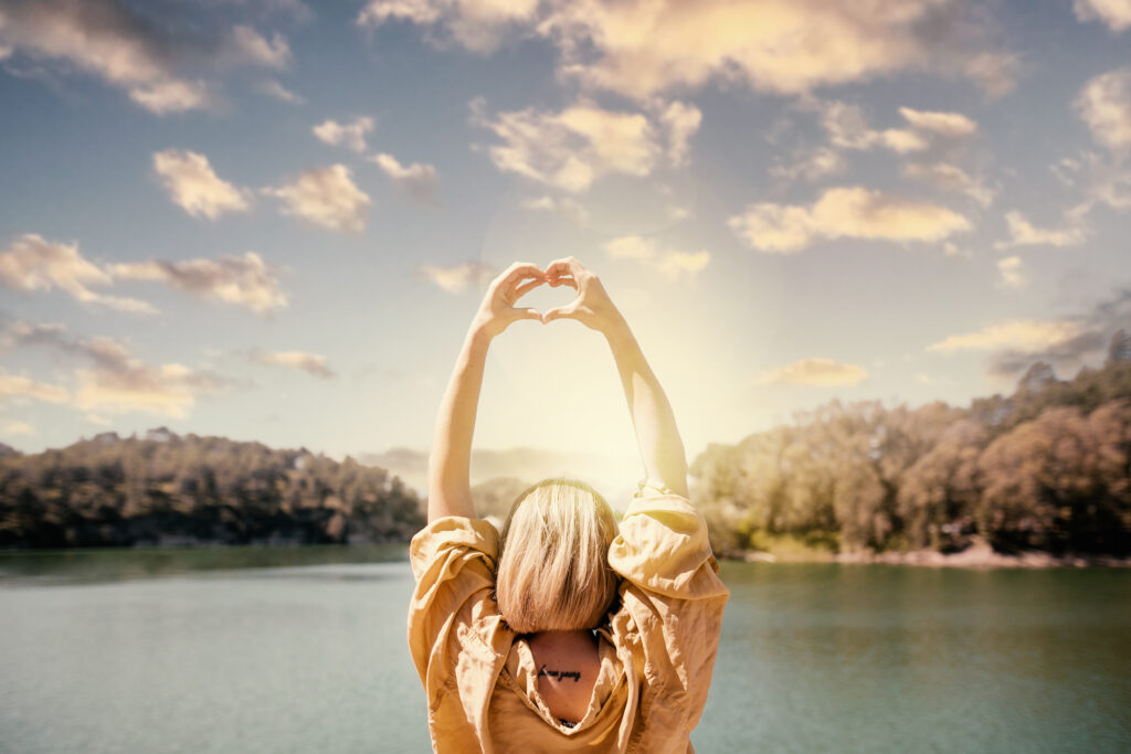 back-view-woman-making-heart-shaped-hands-sunset